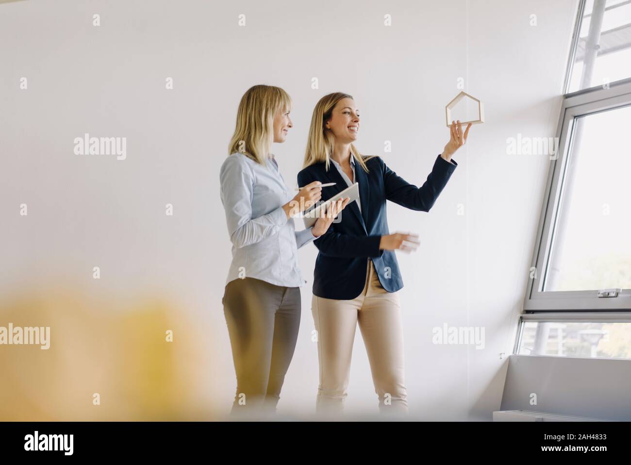 Two young businesswomen with tablet and house model talking in office Stock Photo