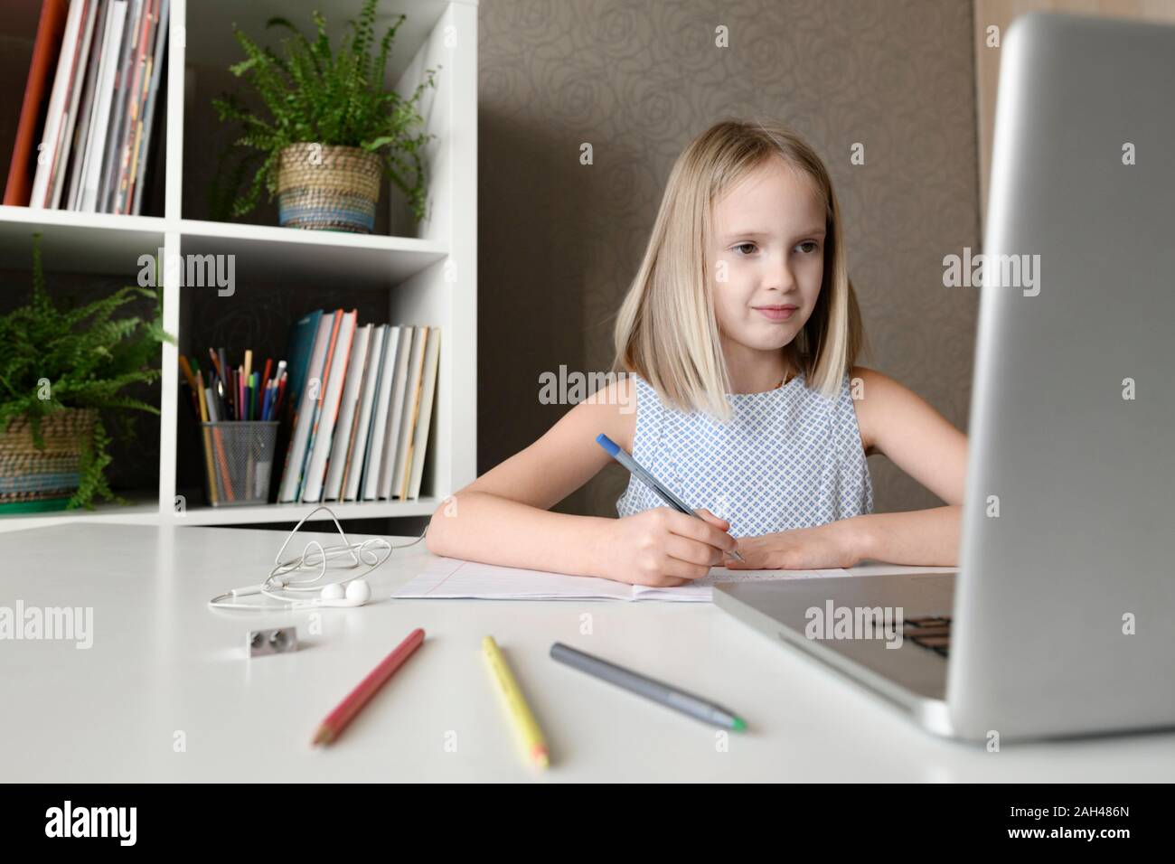 Girl sitting at table at home doing homework and using laptop Stock Photo