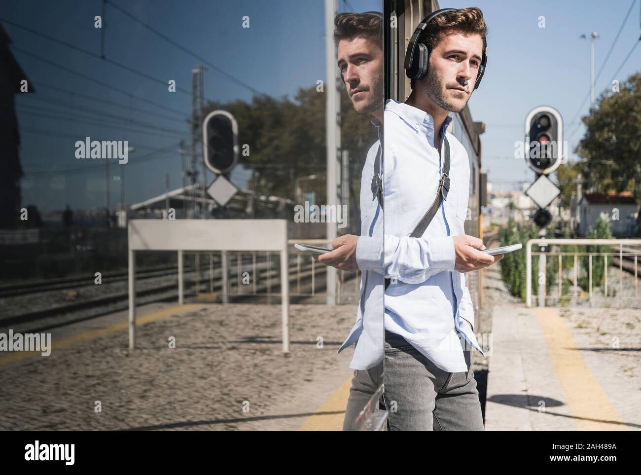 Young man with headphones and smartphone standing in train door Stock Photo
