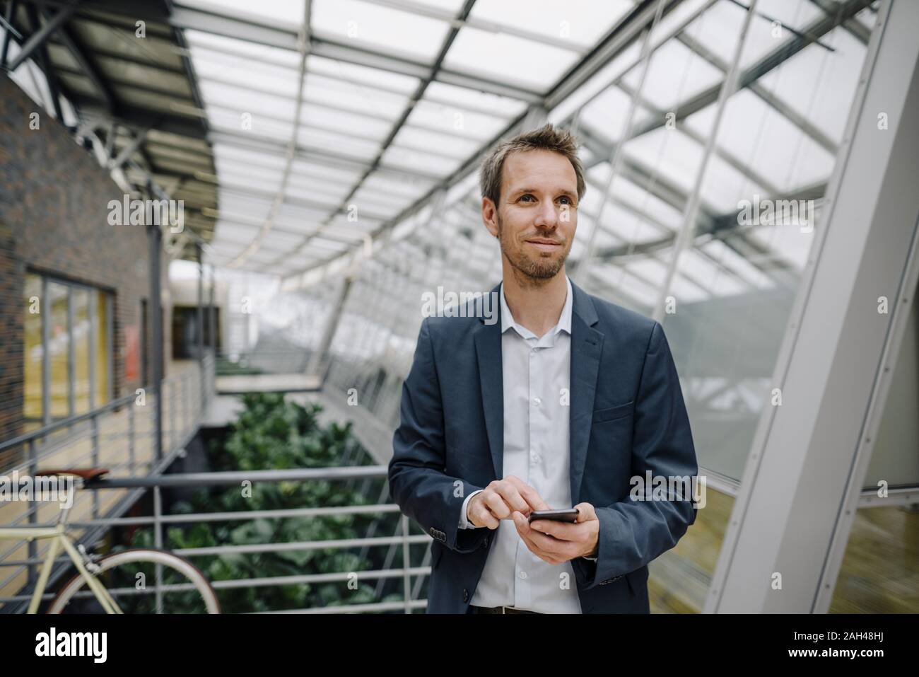 Smiling businessman using cell phone in modern office building Stock Photo