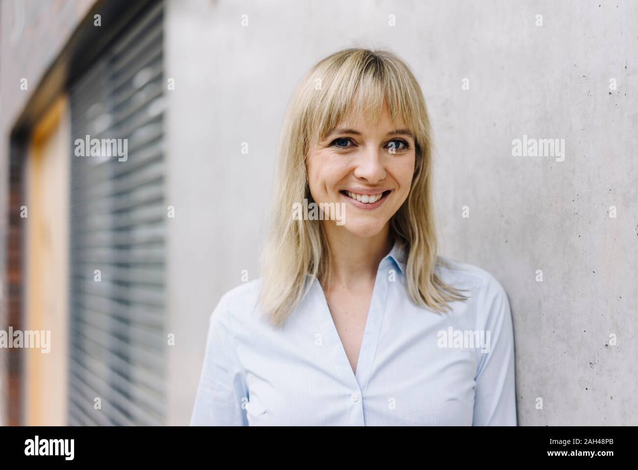 Portrait of a smiling young businesswoman leaning against a wall Stock Photo