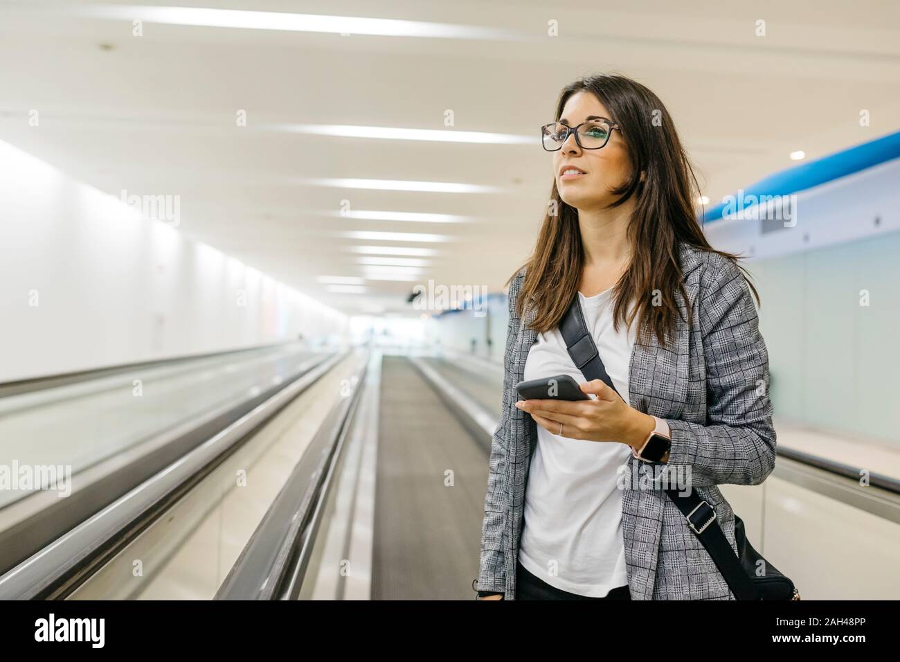 Young businesswoman using smartphone on moving walkway Stock Photo