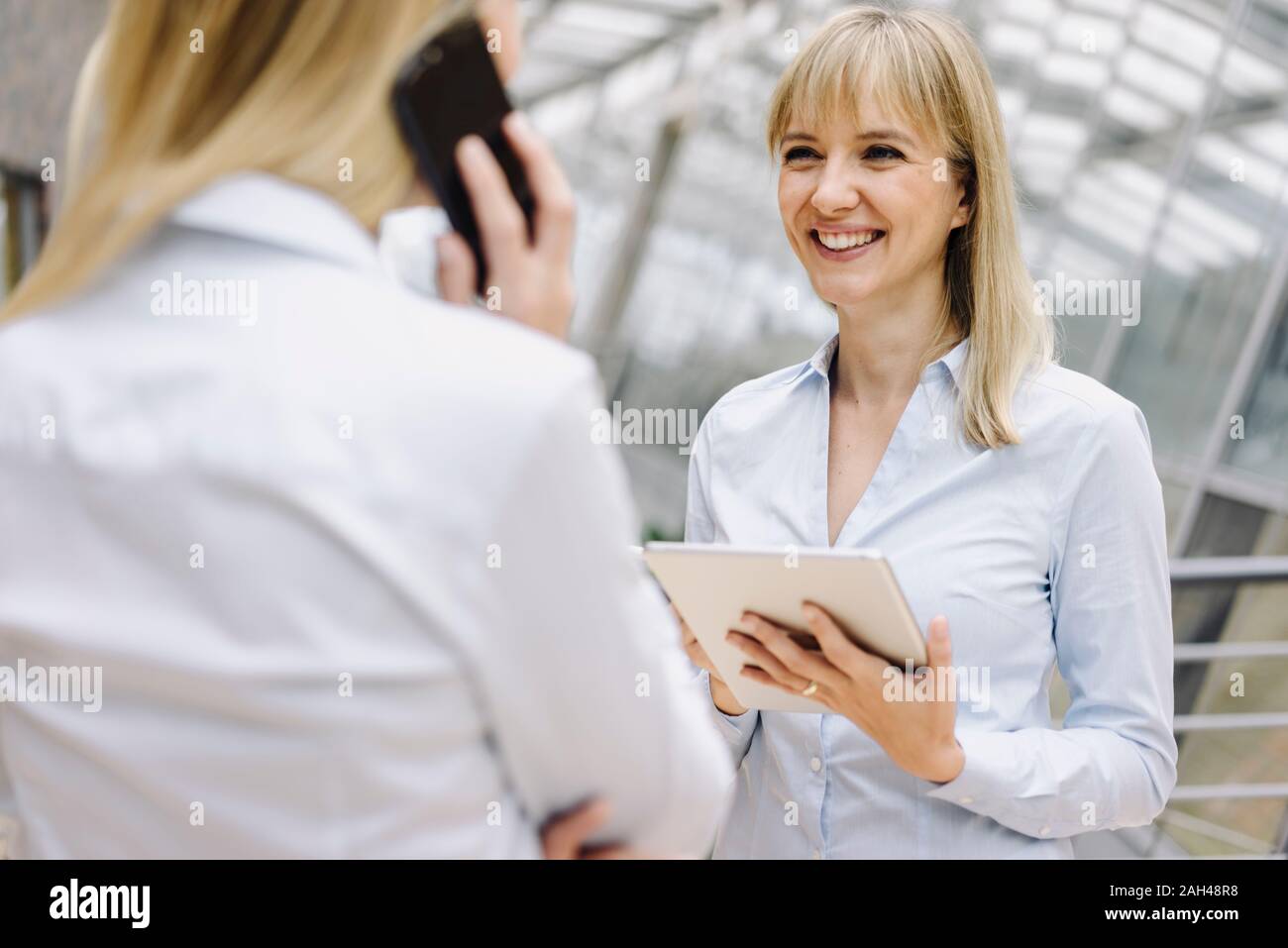 Portrait of young businesswoman with tablet smiling at colleague in office Stock Photo