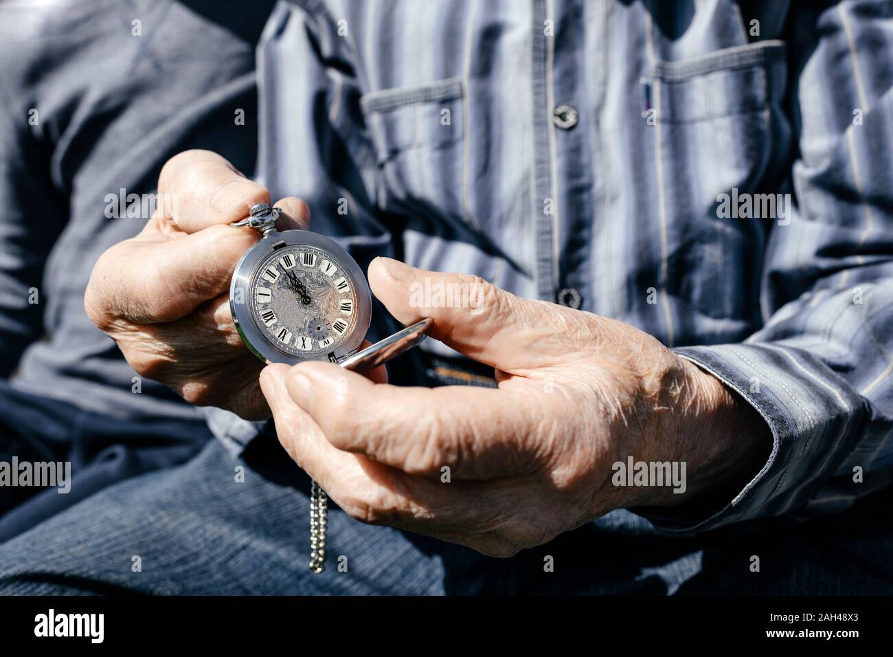 Old man's hands holding silver pocket clock, close-up Stock Photo