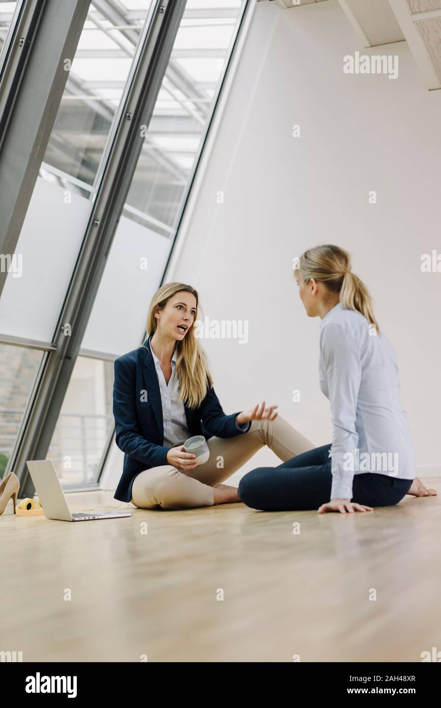 Two young businesswomen sitting on the floor and talking in office Stock Photo