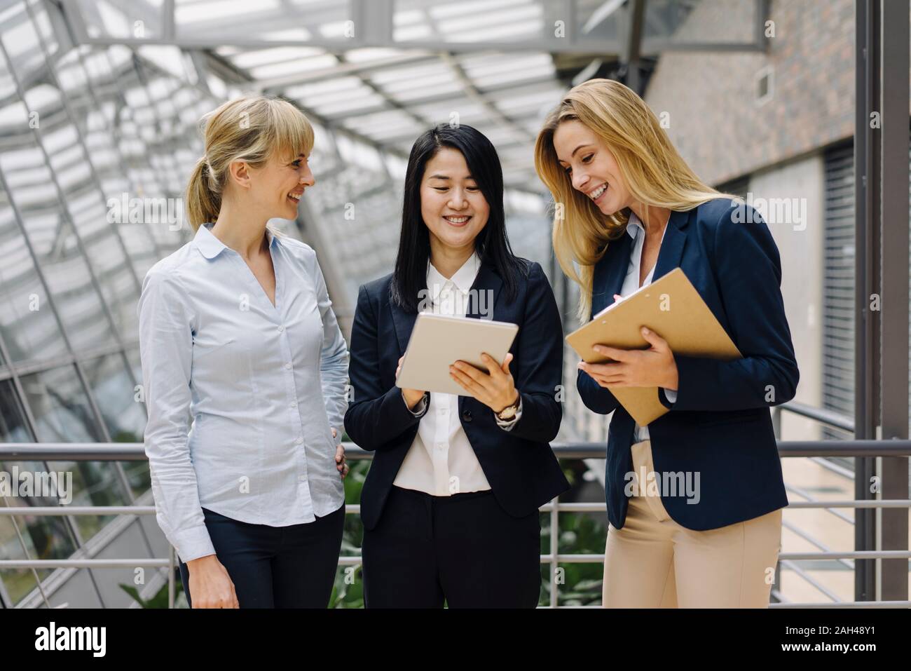 Three businesswomen with tablet talking in modern office building Stock Photo