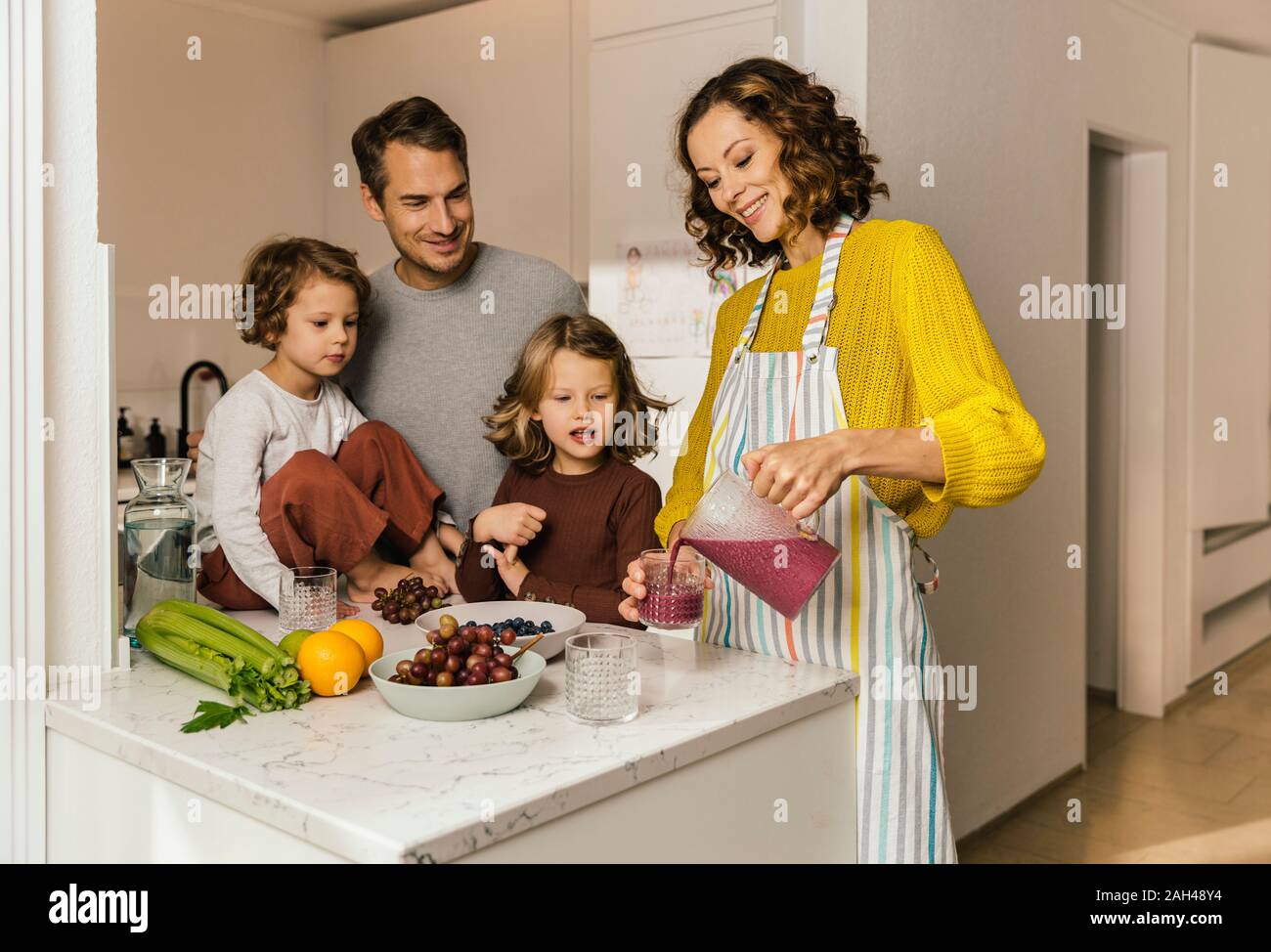 Mother preparing a smoothie for her family in kitchen Stock Photo