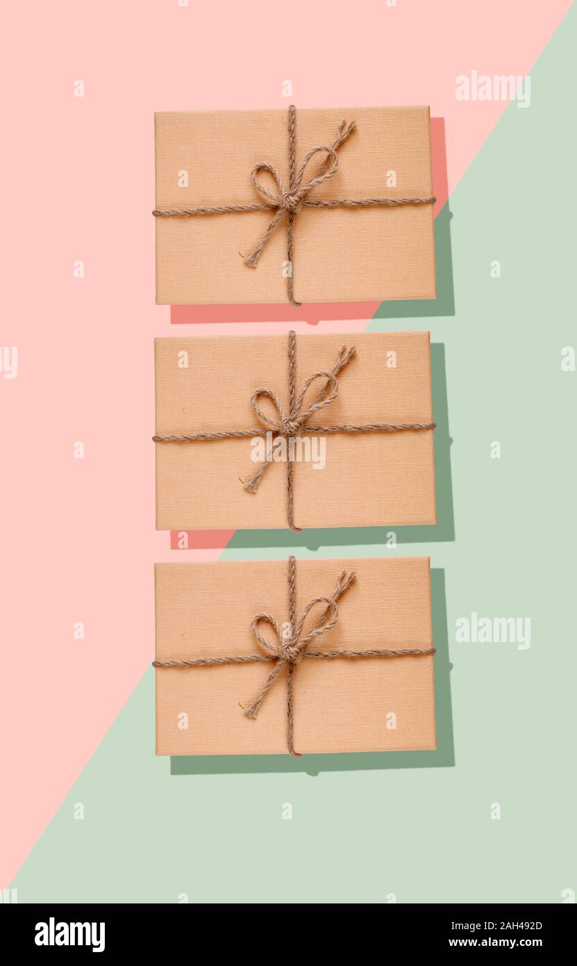 Three eco-friendly presents in a cardboard boxes decorated with a rope bow on green and pastel pink background Stock Photo