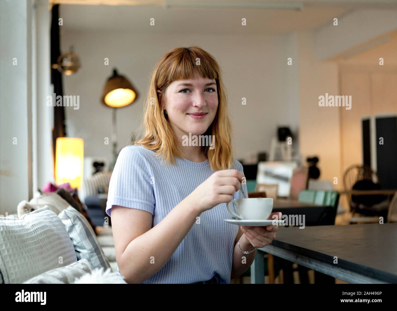 Portrait of strawberry blonde young woman with nose piercing with cup of coffee in a cafe Stock Photo
