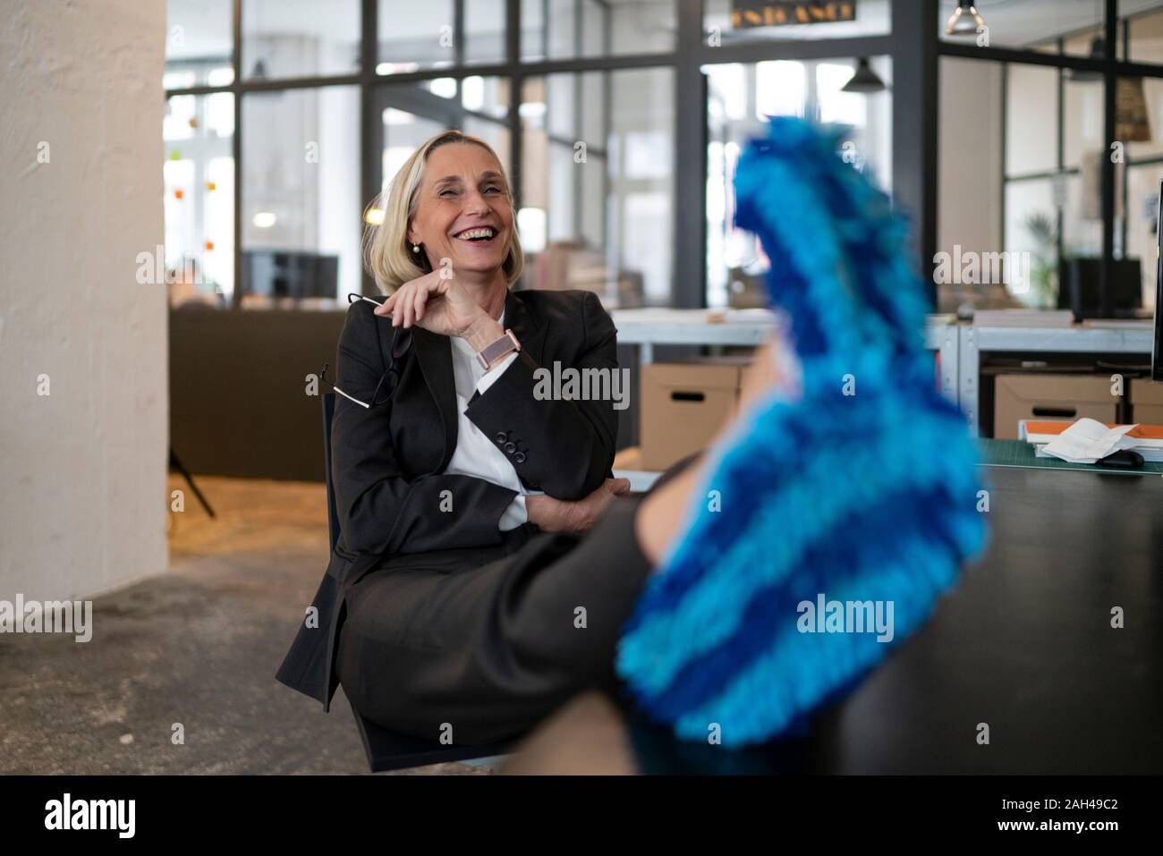 Laughing mature businesswoman with feet on desk wearing cleansing slippers in office Stock Photo
