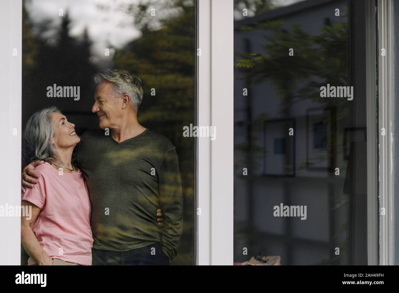 Happy senior couple behind windowpane of their home Stock Photo