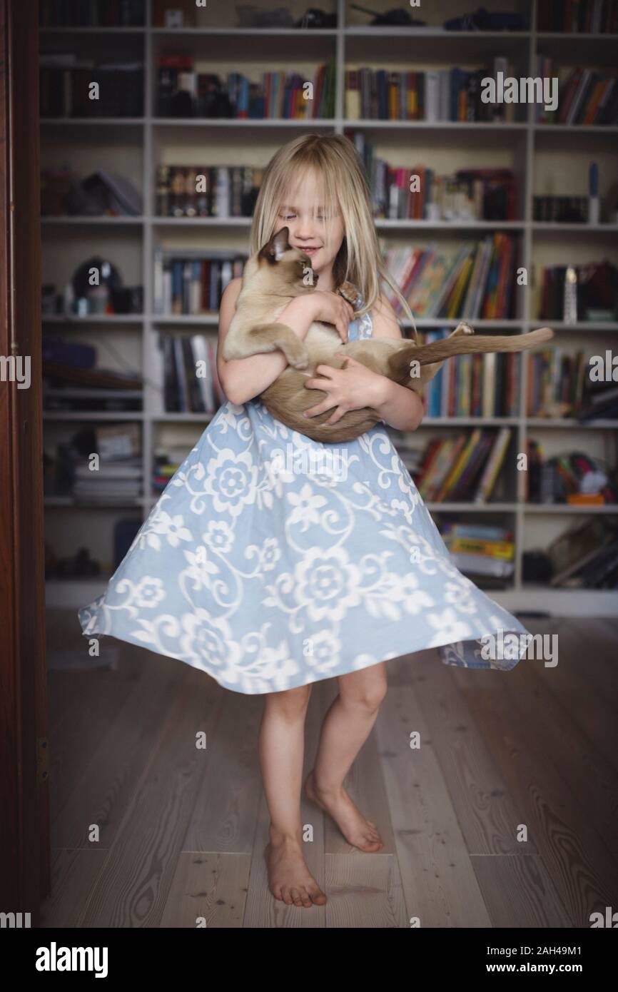 Blond little girl dancing with her Burmese cat at home Stock Photo