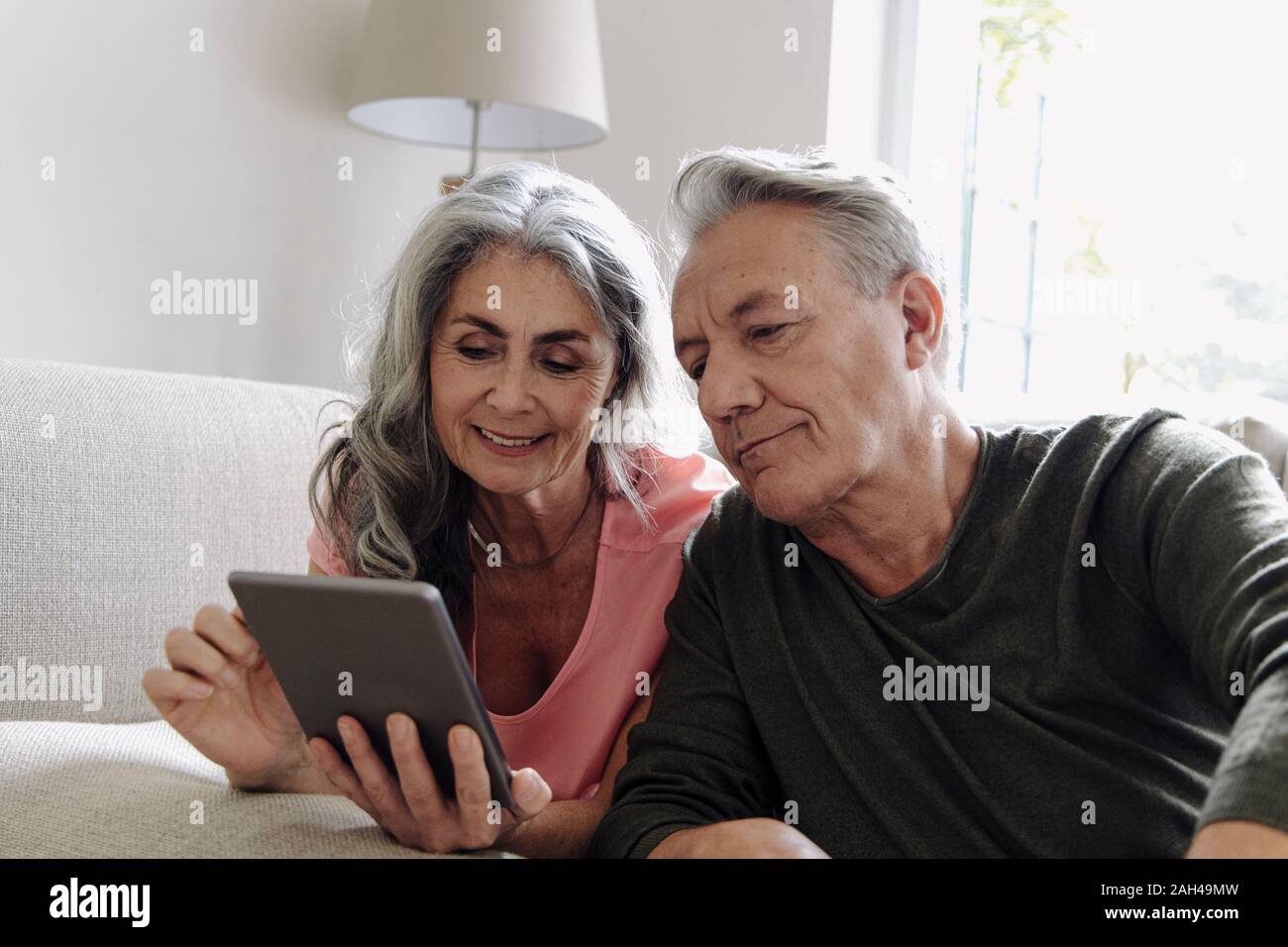 Happy senior couple relaxing on couch at home using tablet Stock Photo