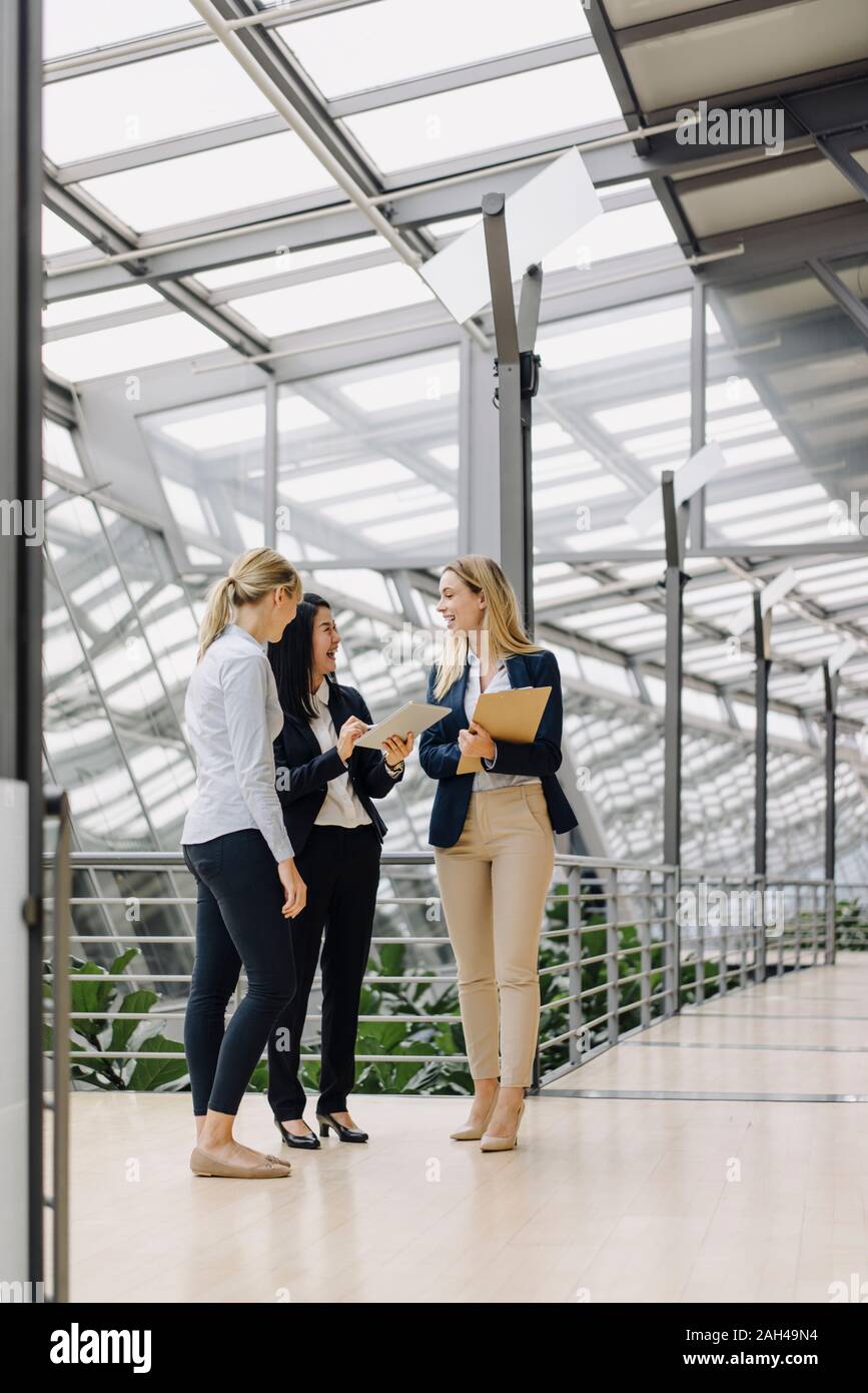 Three happy businesswomen with tablet talking in modern office building Stock Photo