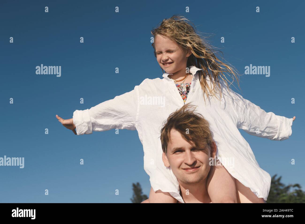Father carrying his little daughter on shoulders under blue sky Stock Photo