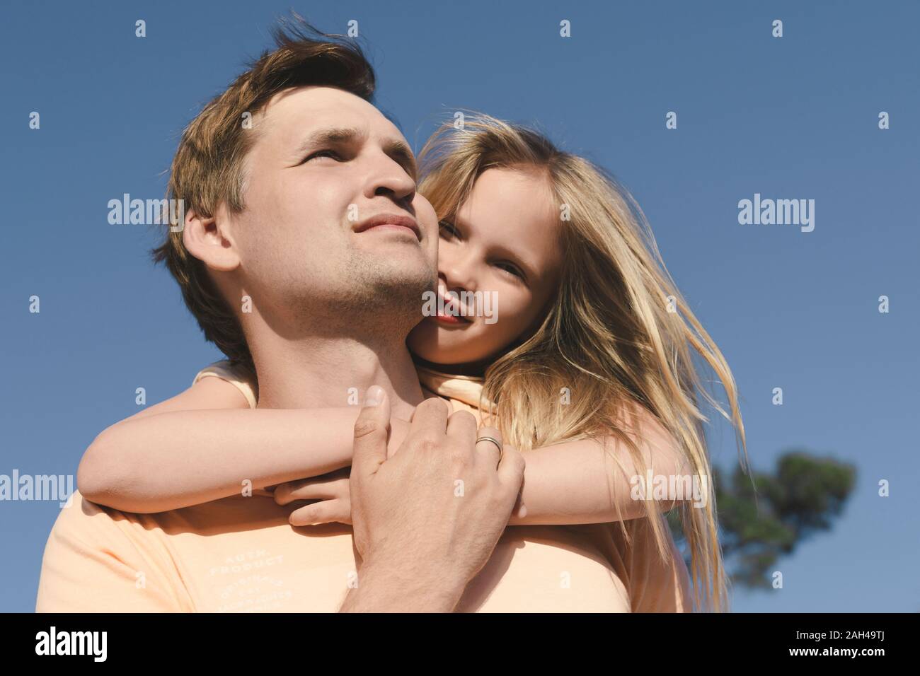 Father carrying his little daughter piggyback under blue sky Stock Photo