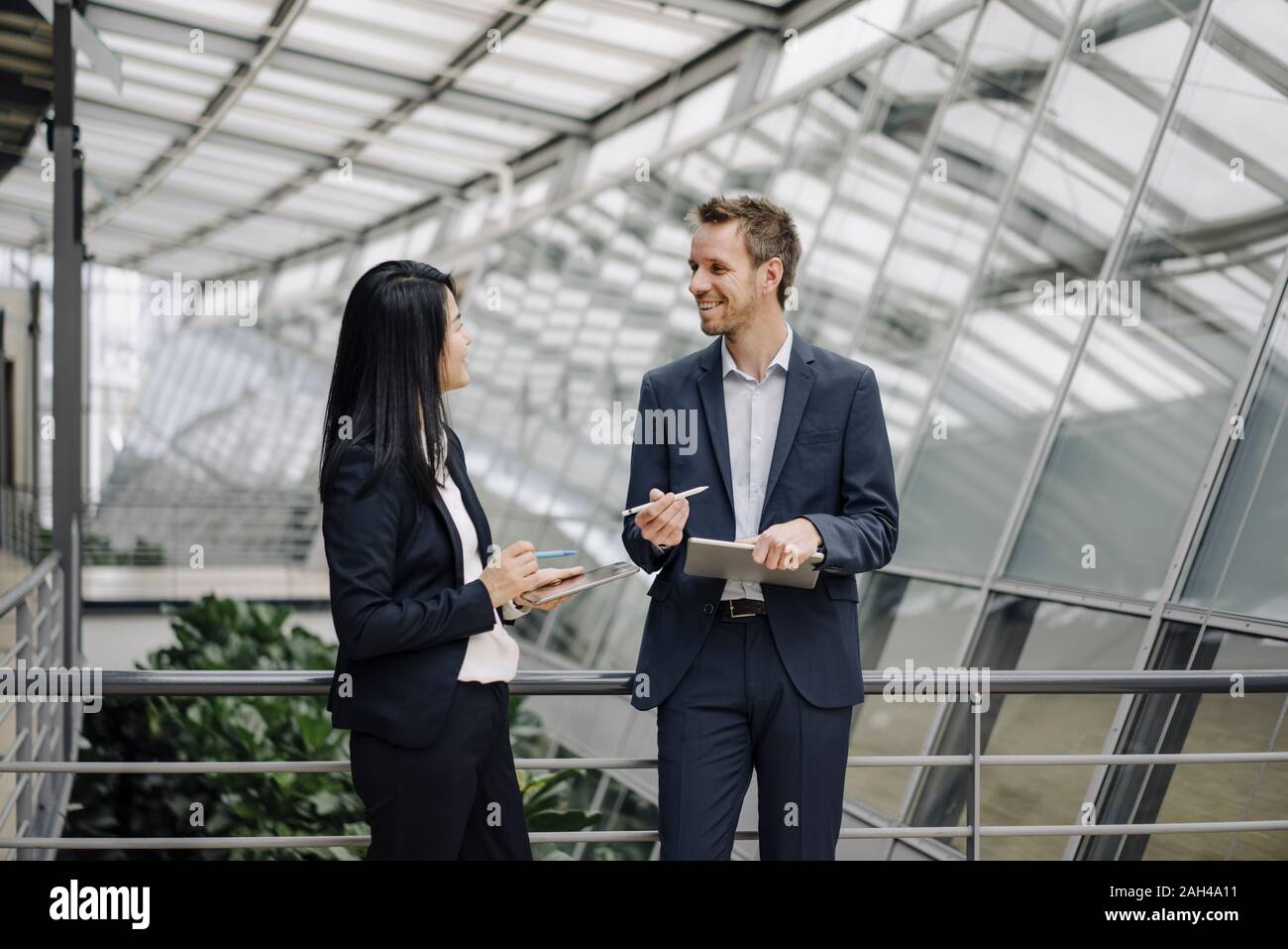 Smiling businessman and businesswoman with tablets talking in modern office building Stock Photo
