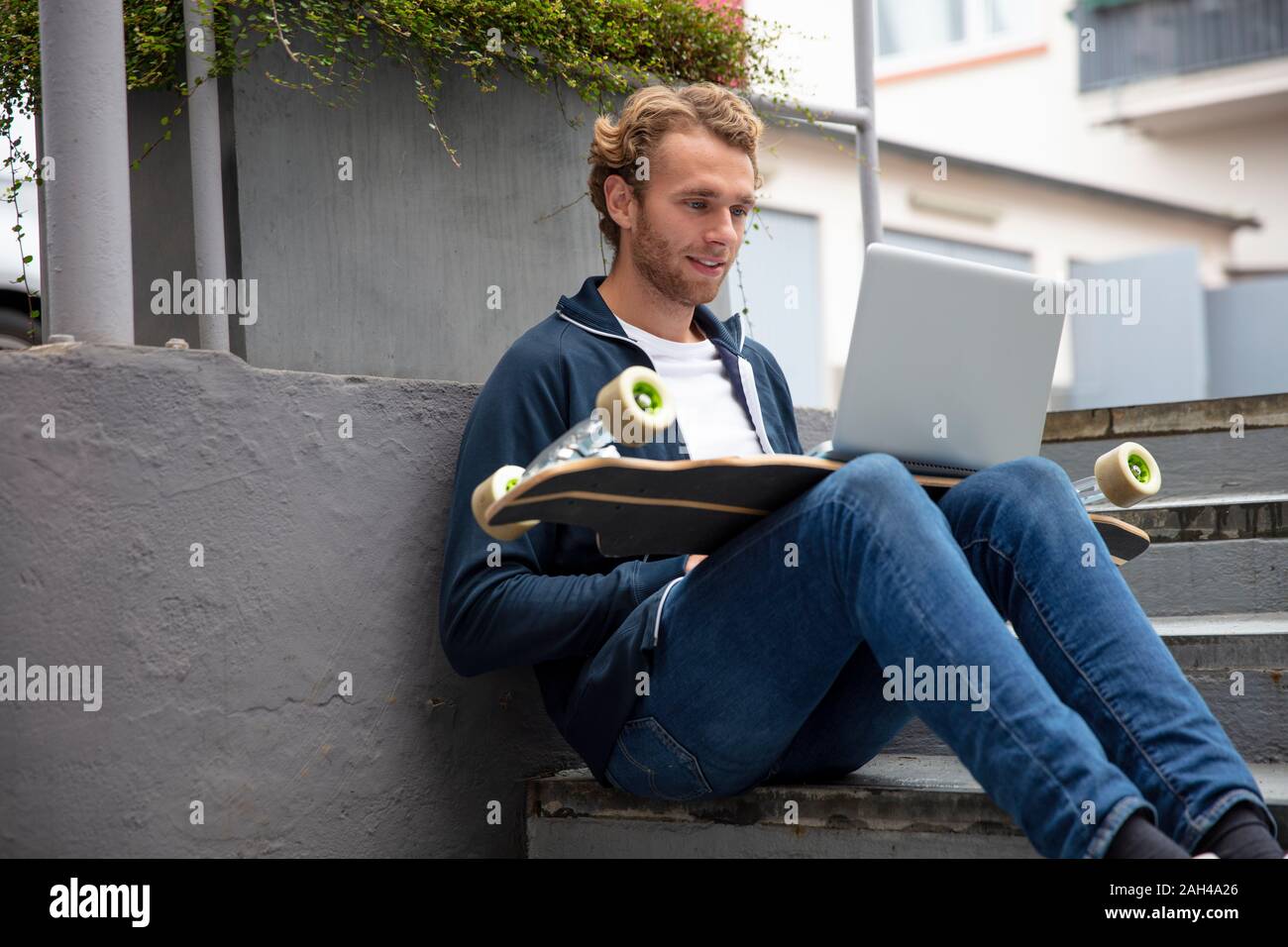 Young man sitting on steps, using laptop on longboard Stock Photo