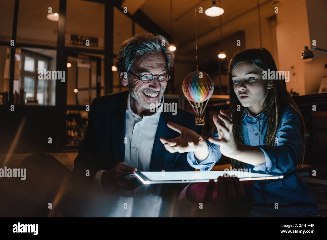 Happy senior buisinessman and girl with hot-air balloon and shining tablet in office Stock Photo