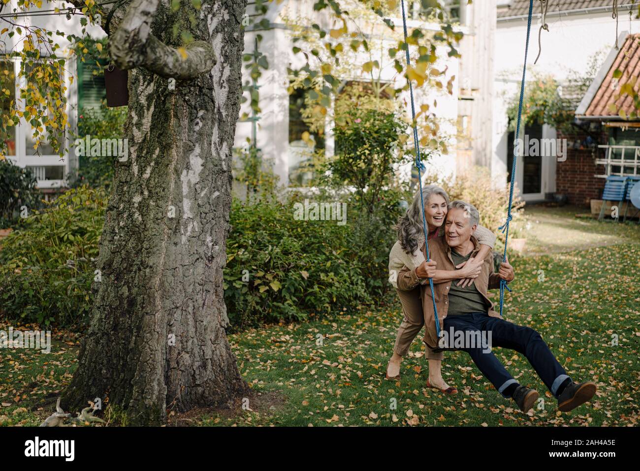 Happy woman embracing senior man on a swing in garden Stock Photo
