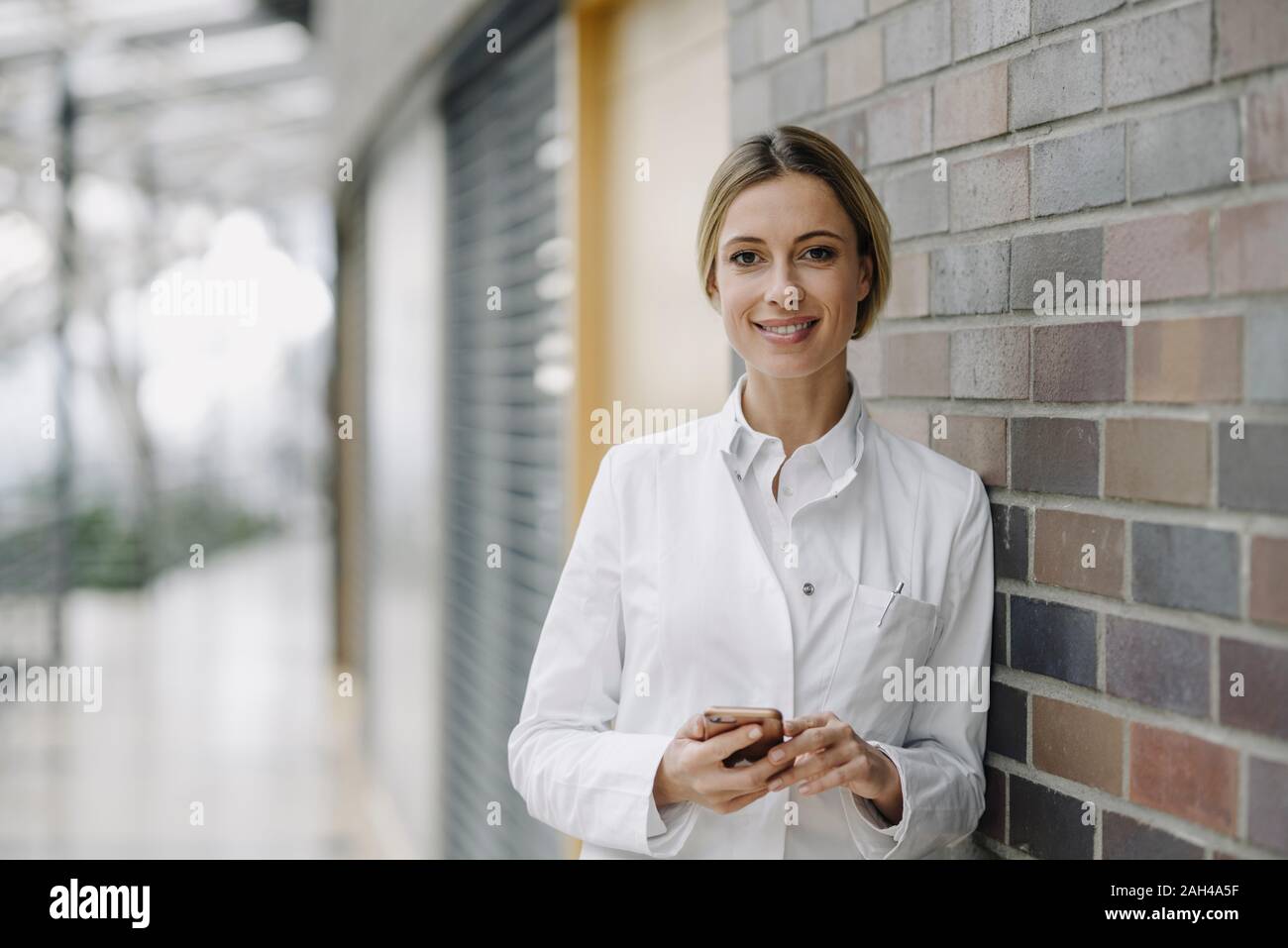 Portrait of a confident female doctor leaning against a brick wall Stock Photo