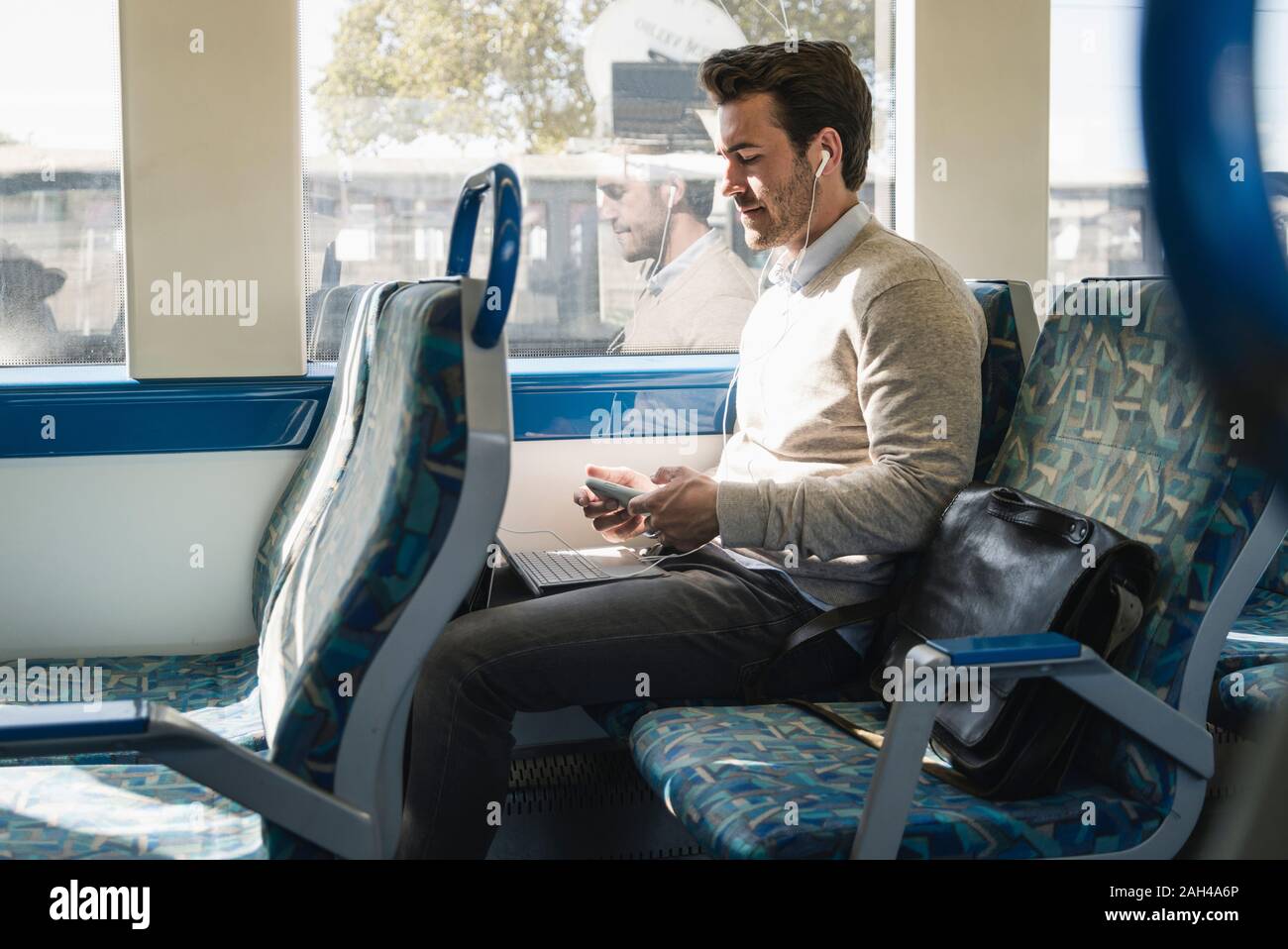 Young man with earphones using smartphone and tablet on a train Stock Photo