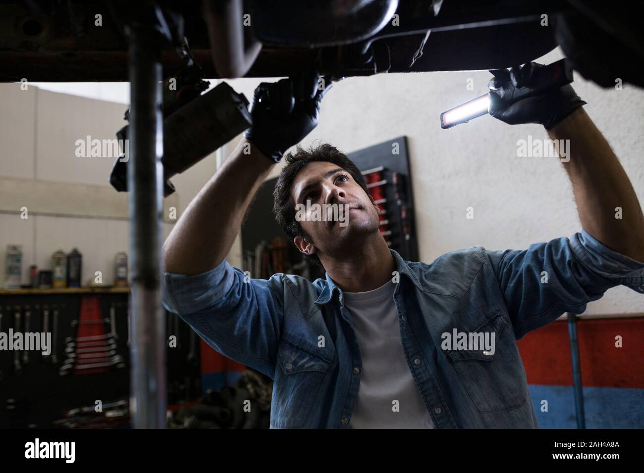 Man in shirt standing under car and fixing with tool working in service Stock Photo