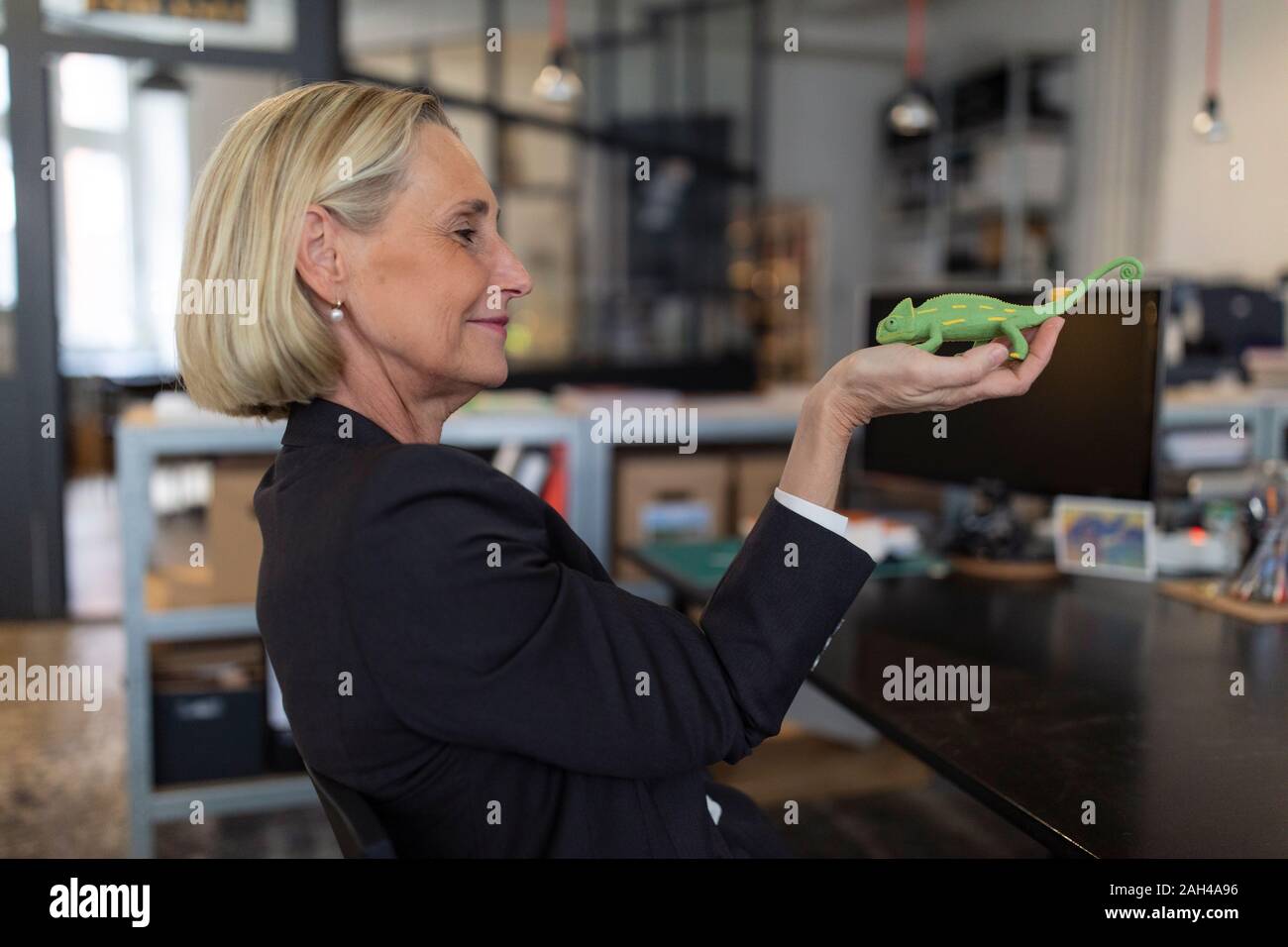 Mature businesswoman holding chameleon figurine in office Stock Photo