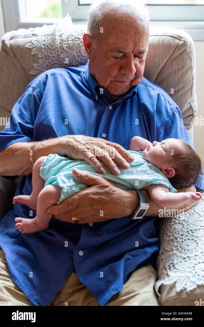 Grandfather sitting in an armchair holding a newborn baby Stock Photo