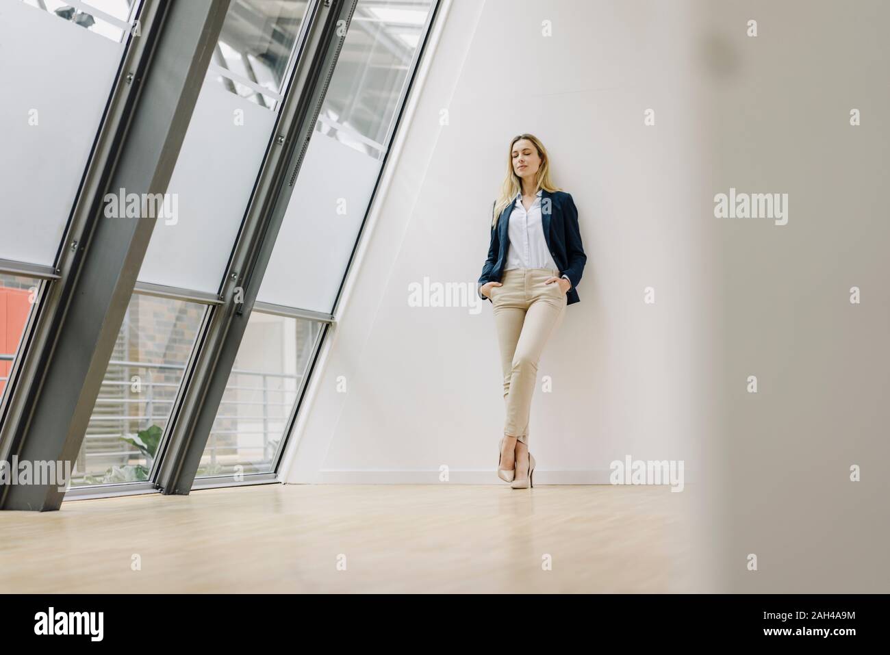 Young businesswoman leaning against a wall in a modern office building Stock Photo