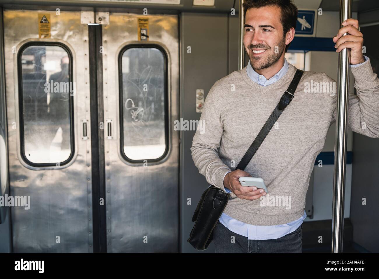 Smiling young man with smartphone on a train Stock Photo