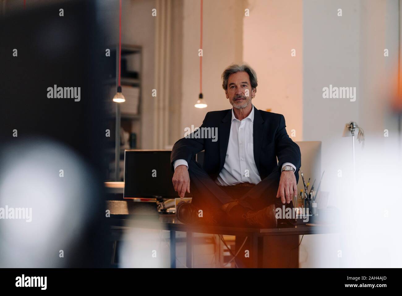 Senior businessman sitting cross-legged on desk in office Stock Photo ...