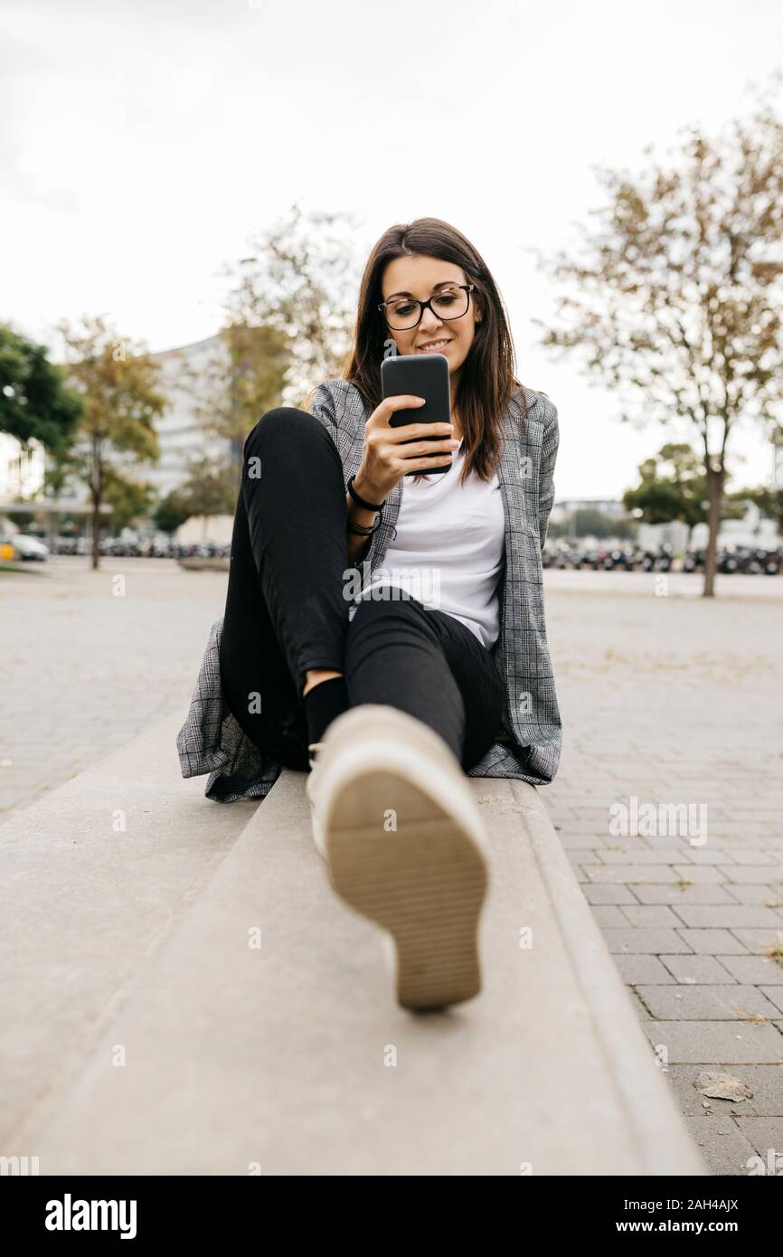 Young businesswoman using smartphone, sitting on bench in the city Stock Photo