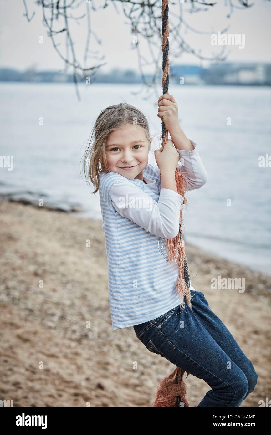 Portrait of smiling little girl swinging with rope at riverside Stock Photo