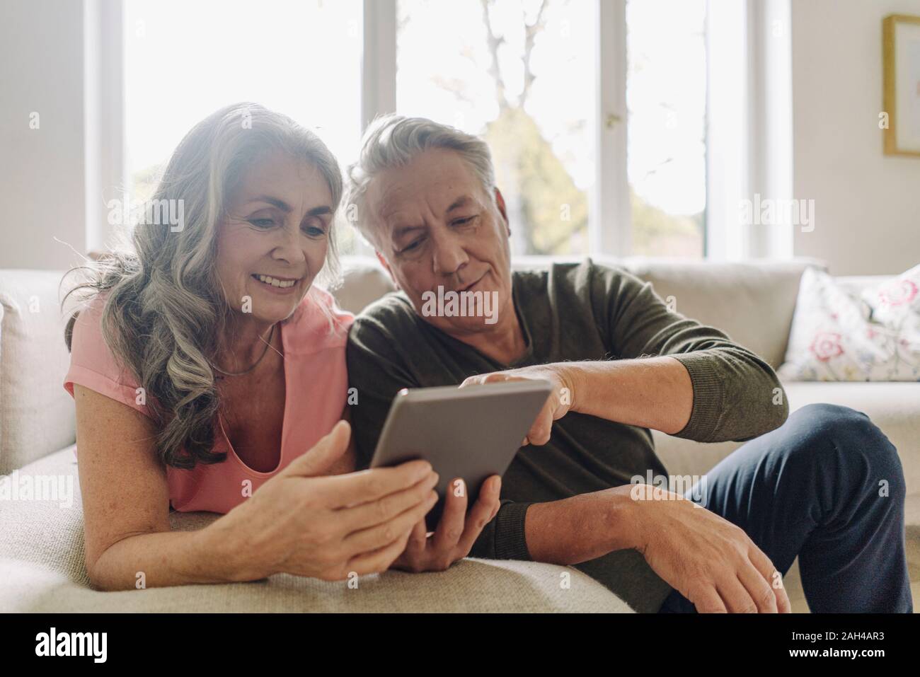 Happy senior couple relaxing on couch at home using tablet Stock Photo