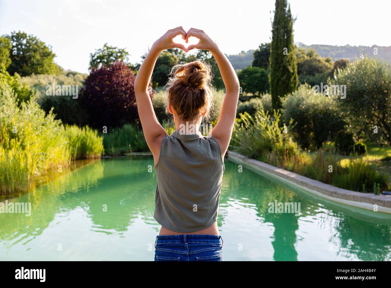 Rear view of a girl standing at swimming pool, forming a heart with her hands Stock Photo