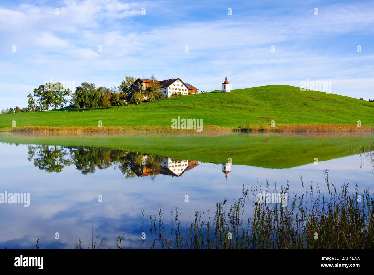 Germany, Bavaria, Halblech, Chapel and farmhouse reflecting in Hegratsrieder See lake Stock Photo