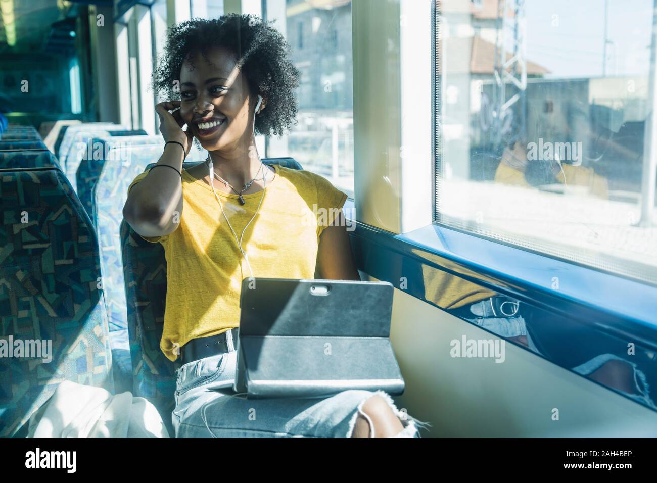 Happy young woman with earphones and tablet on a train Stock Photo