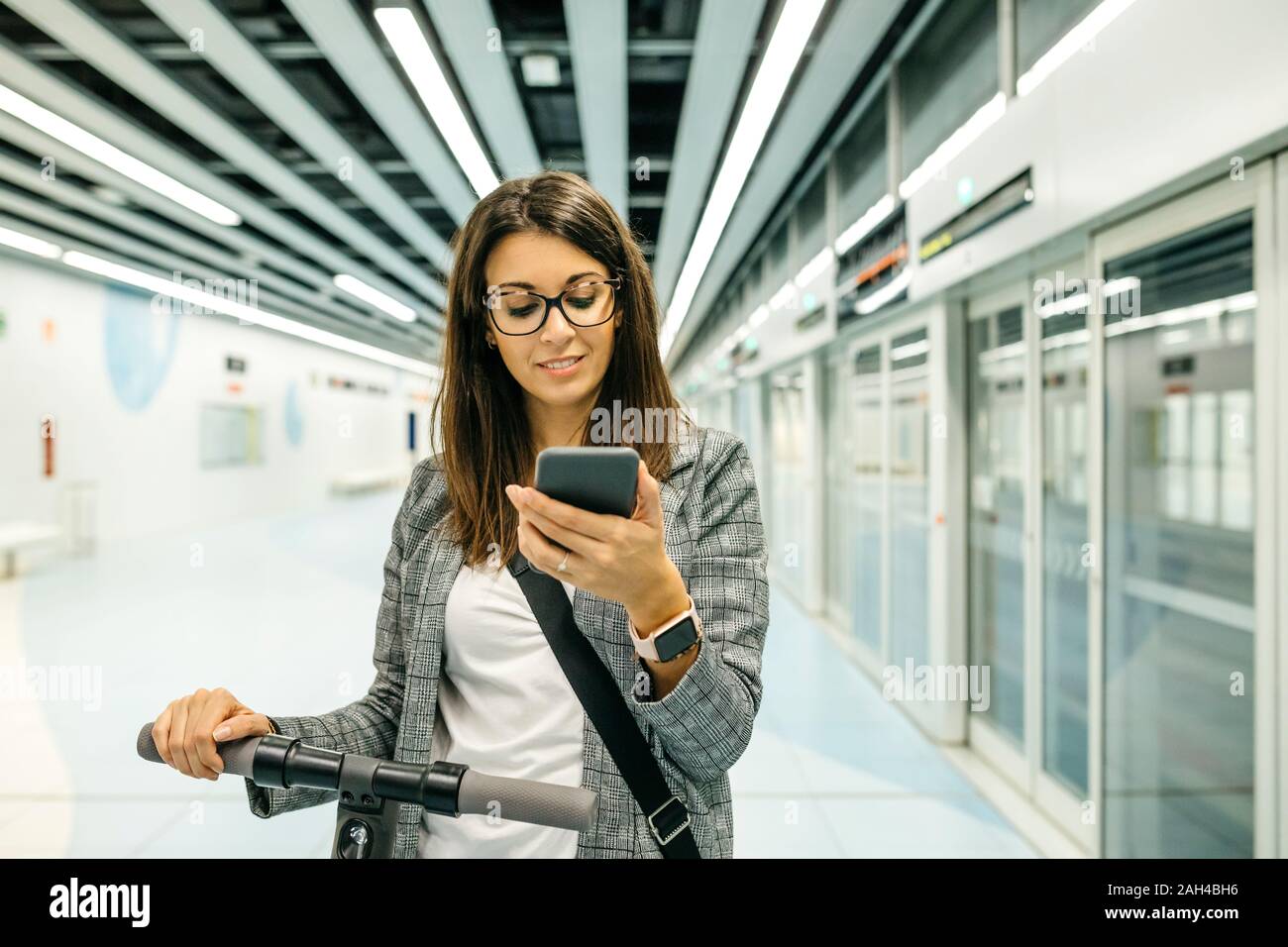 Young businesswoman with e-scooter using the phone at the subway station Stock Photo