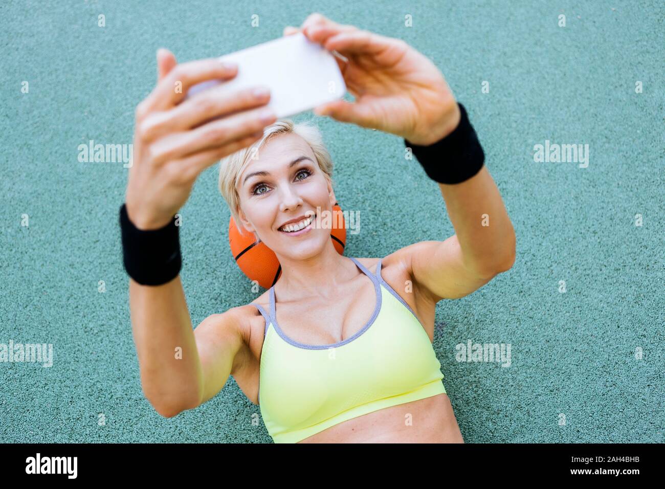 Blonde woman lying on basketball and taking a selfie Stock Photo