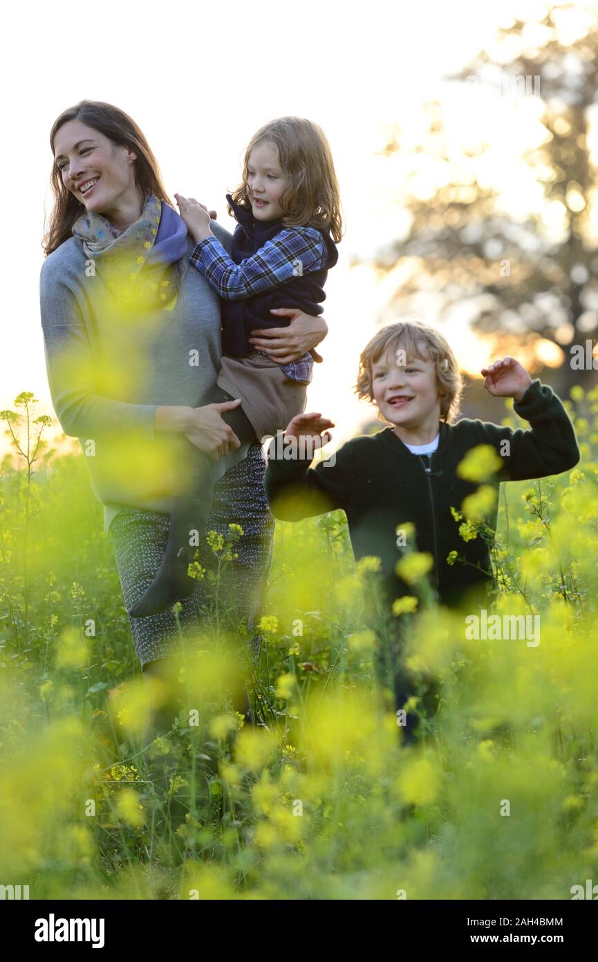 Mother carrying her daughter, walking with son over flower meadow Stock Photo