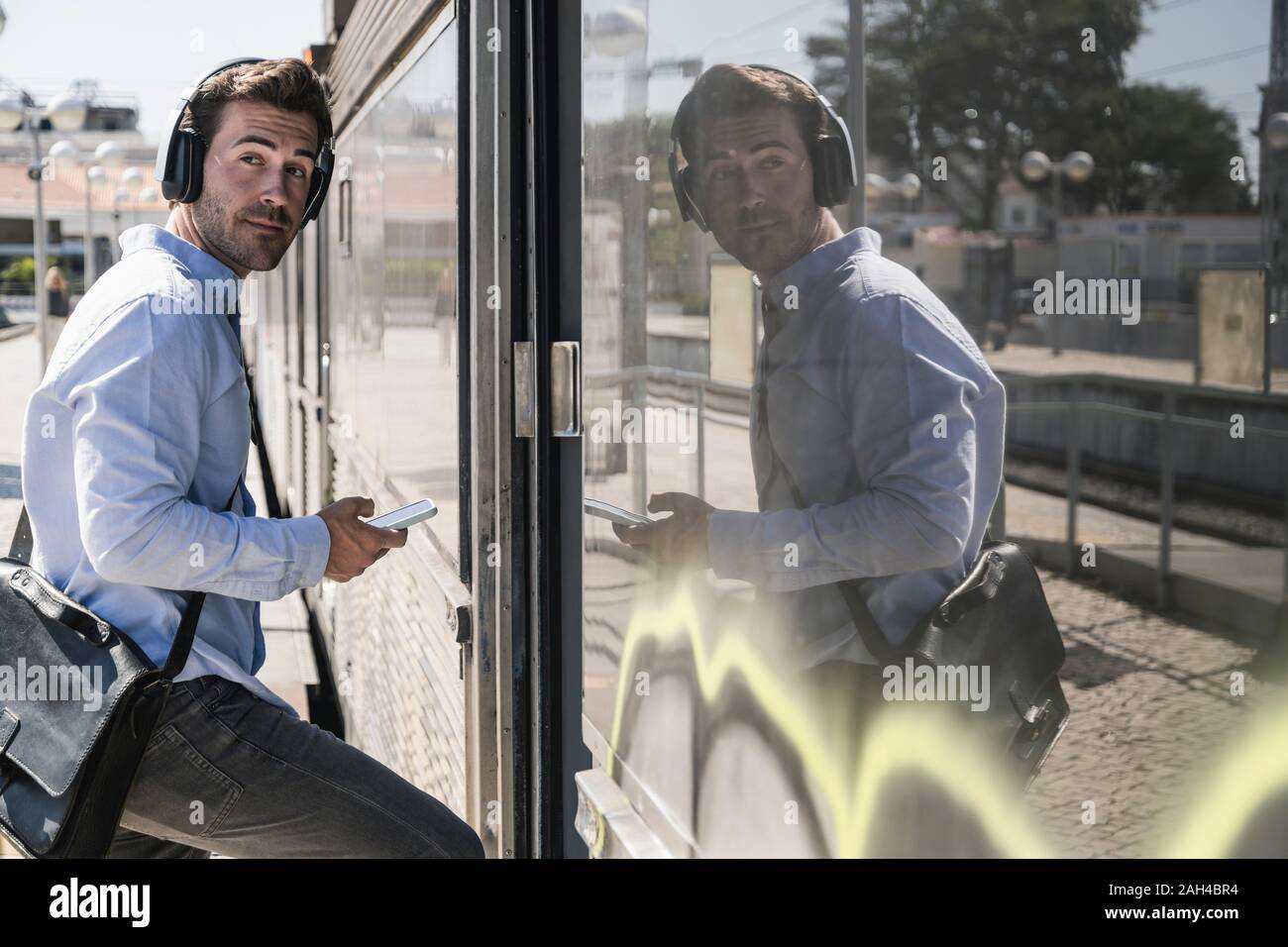 Young man with headphones and smartphone entering a train Stock Photo