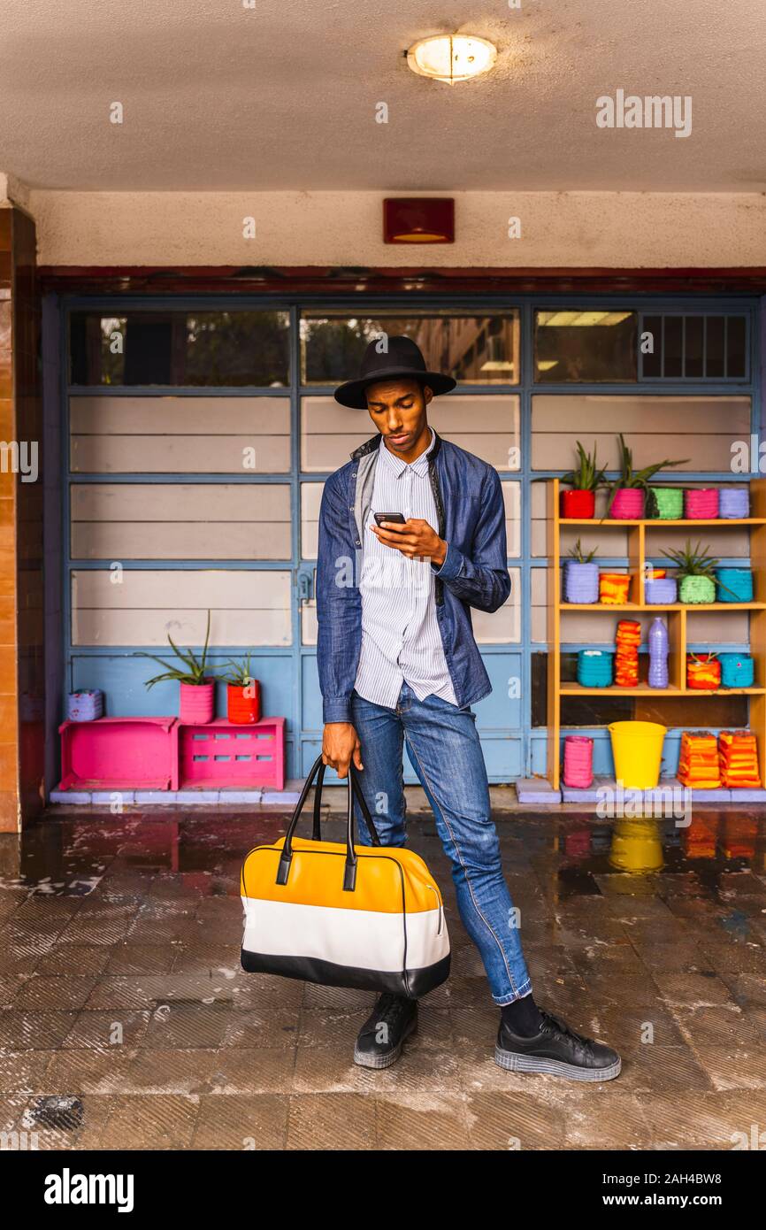 Smiling young man with bag using smartphone Stock Photo