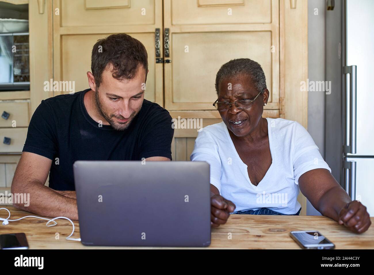 Senior woman and man sitting at kitchen table sharing laptop Stock Photo