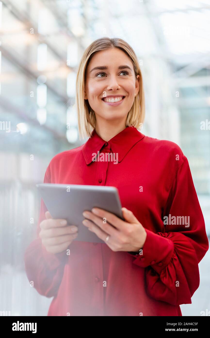 Smiling young businesswoman wearing red shirt using tablet Stock Photo