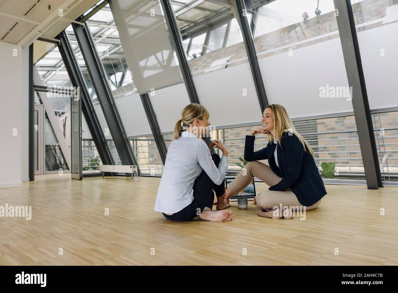Two smiling young businesswomen sitting on the floor and talking in office Stock Photo