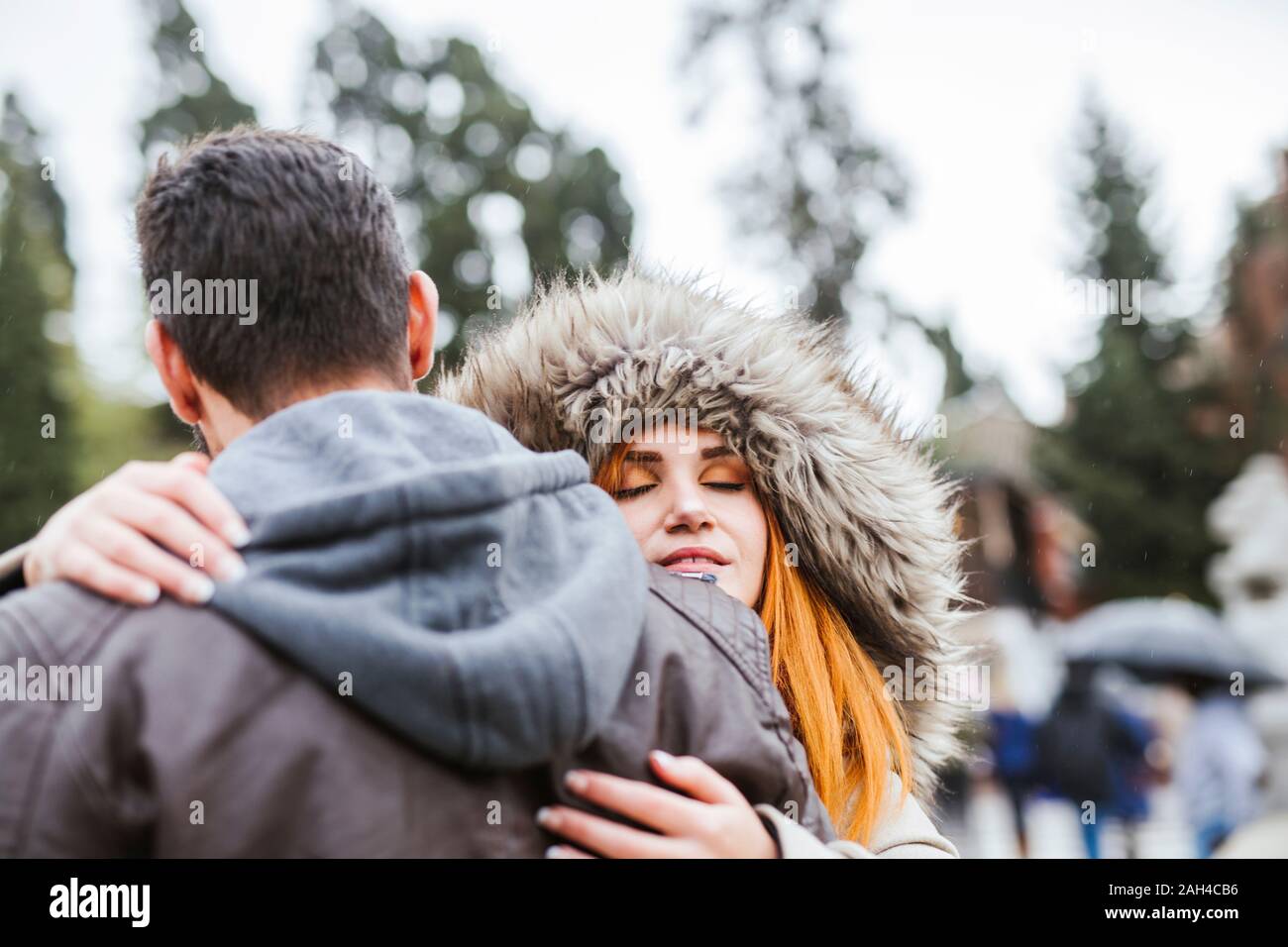 Portrait of young woman with eyes closed hugging her boyfriend outdoors ...