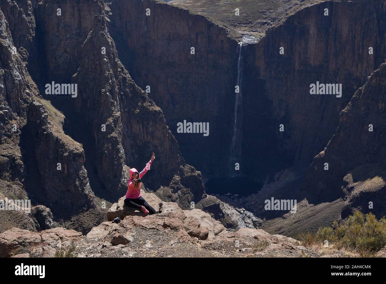 Happy woman sitting on top of a hill at Maletsunyane Falls taking a selfie, Lesotho Stock Photo