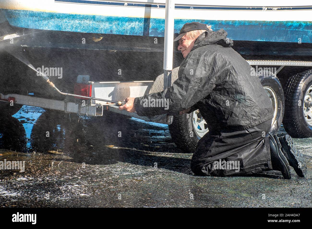 kneeling Caucasian man using pressure washer to clean boat hull Stock Photo