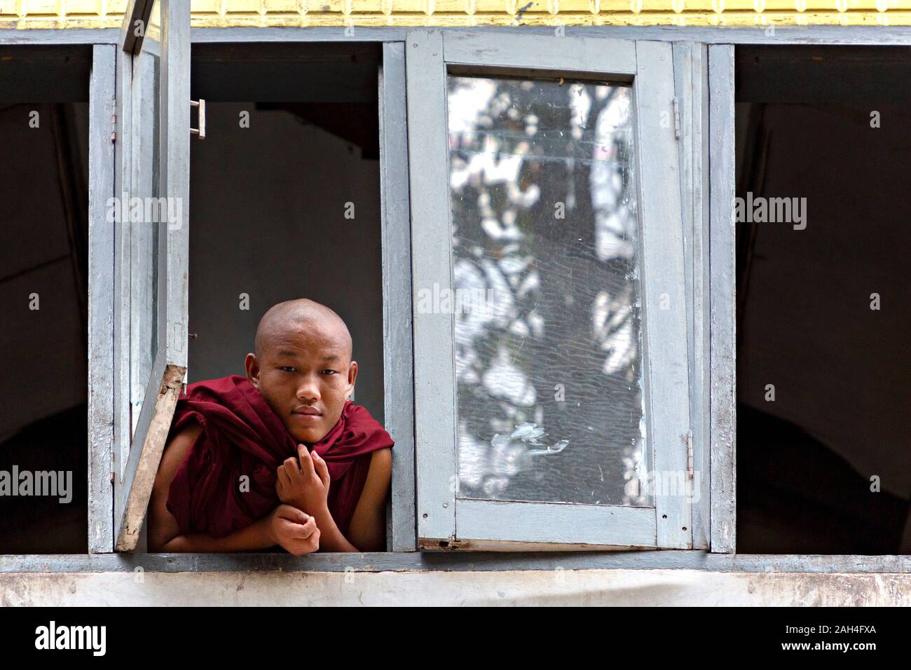 Young monk looking out the window of the dormitory in the monastery, in Yangon, Myanmar Stock Photo